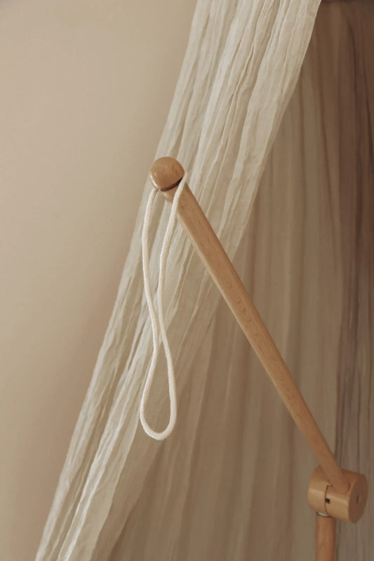 Montant en bois clair avec corde devant un tissu beige, décoration chambre enfant minimaliste.