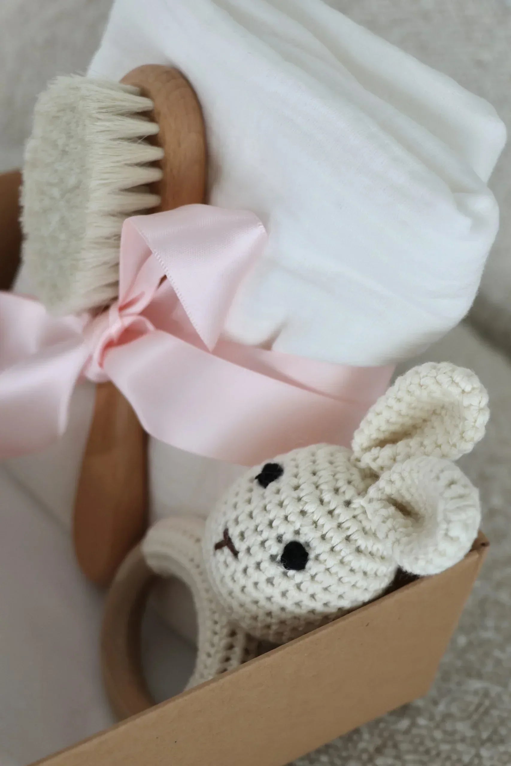 Coffret cadeau bébé avec brosse en bois, doudou lapin crocheté et lange blanc, ruban rose.