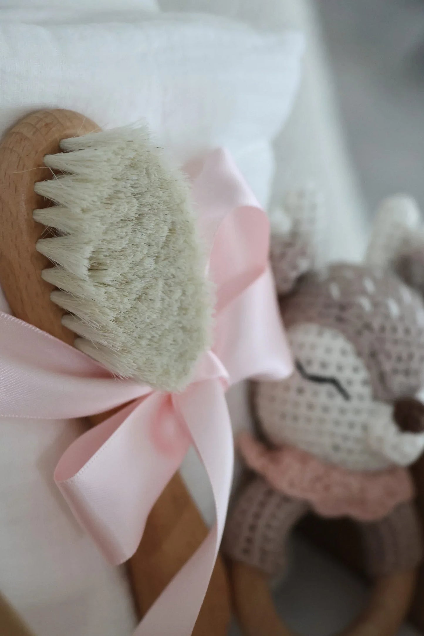 Brosse bébé en bois avec ruban rose, doudou tricoté en arrière-plan, décoration enfant.