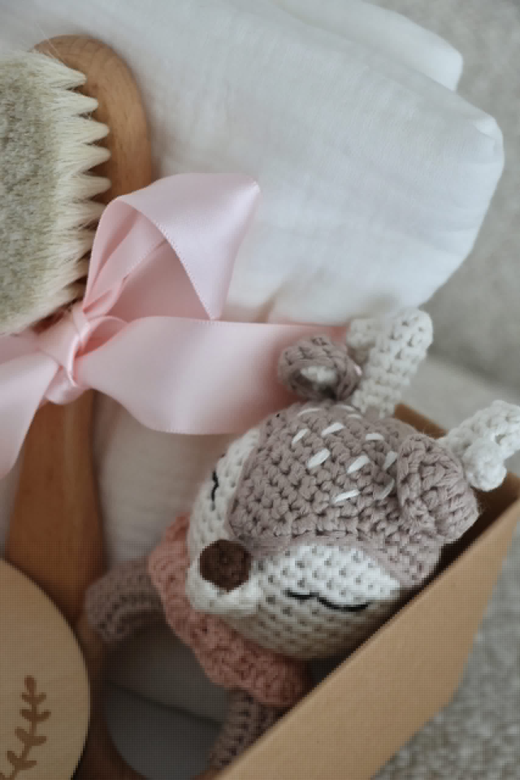 Coffret cadeau bébé avec doudou crochet, brosse douce et lange blanc ruban rose.