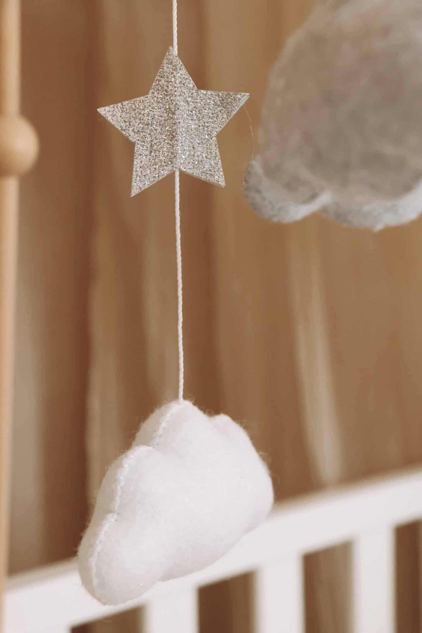 Mobile bébé étoile pailletée et nuage en feutrine blanche suspendus au-dessus d’un lit enfant