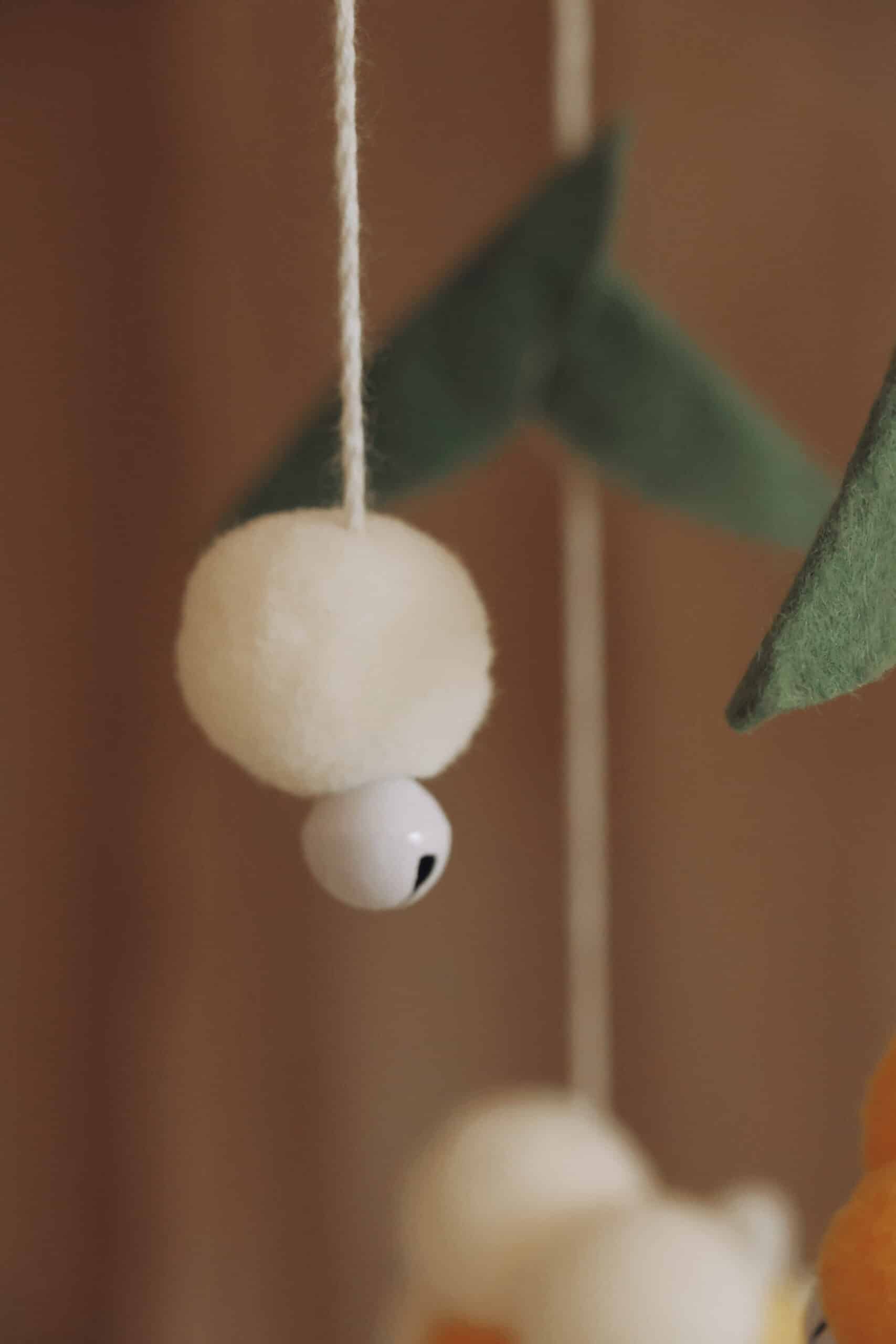 Mobile bébé naturel avec boule de laine blanche, grelot et feuilles en feutrine verte.