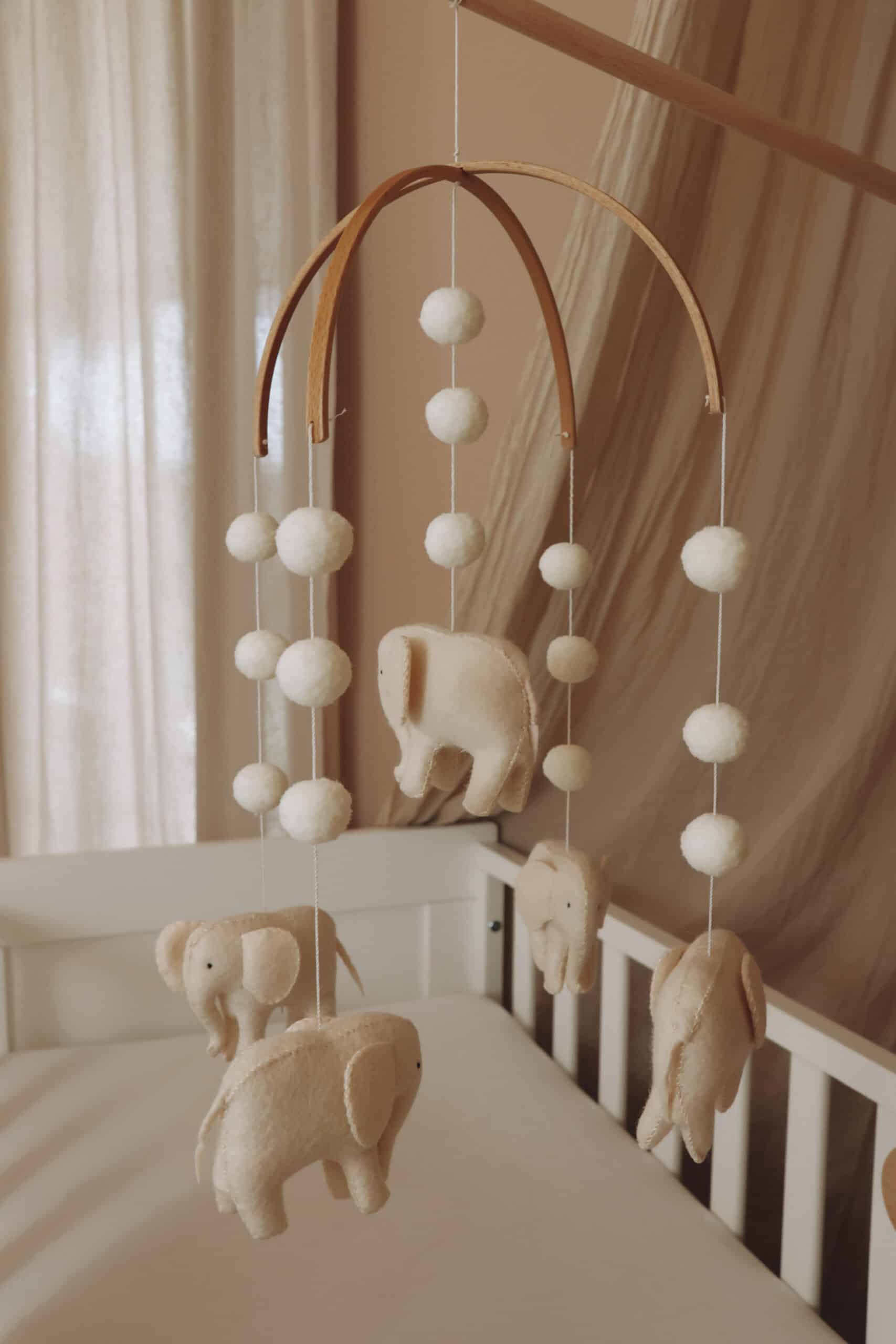 Mobile bébé éléphants en feutrine beige avec boules, suspendu au-dessus d’un lit enfant.