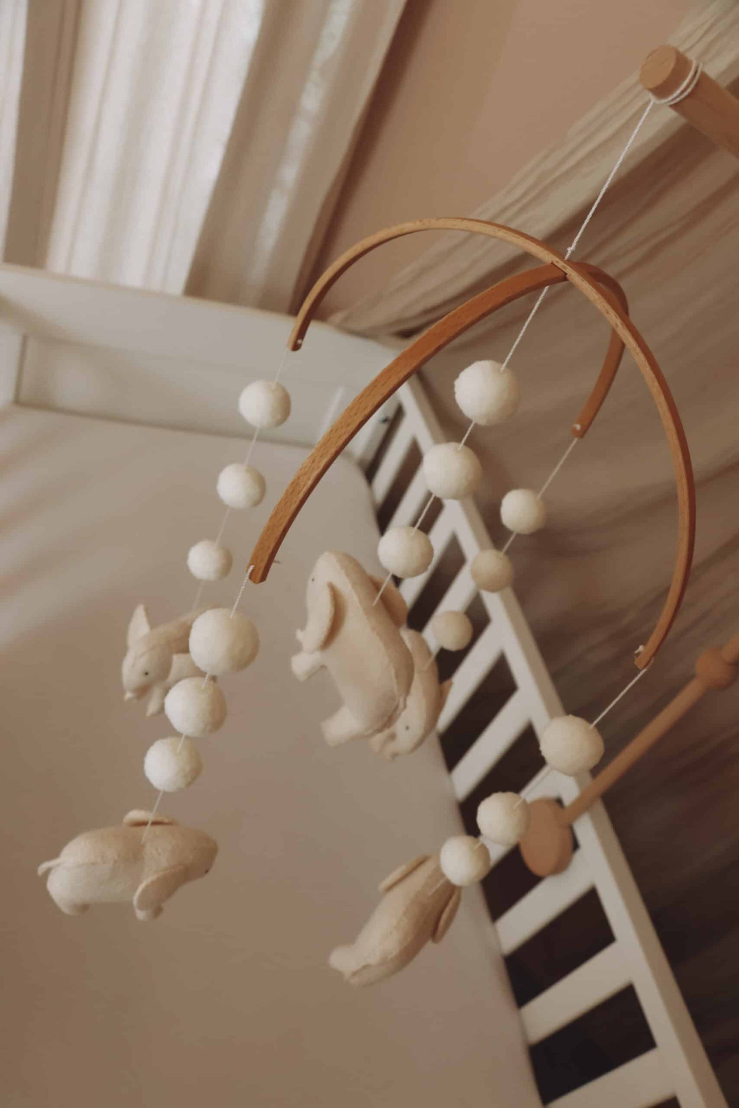 Mobile bébé en feutrine animaux beige, suspendu au-dessus d’un lit à barreaux, décoration chambre enfant