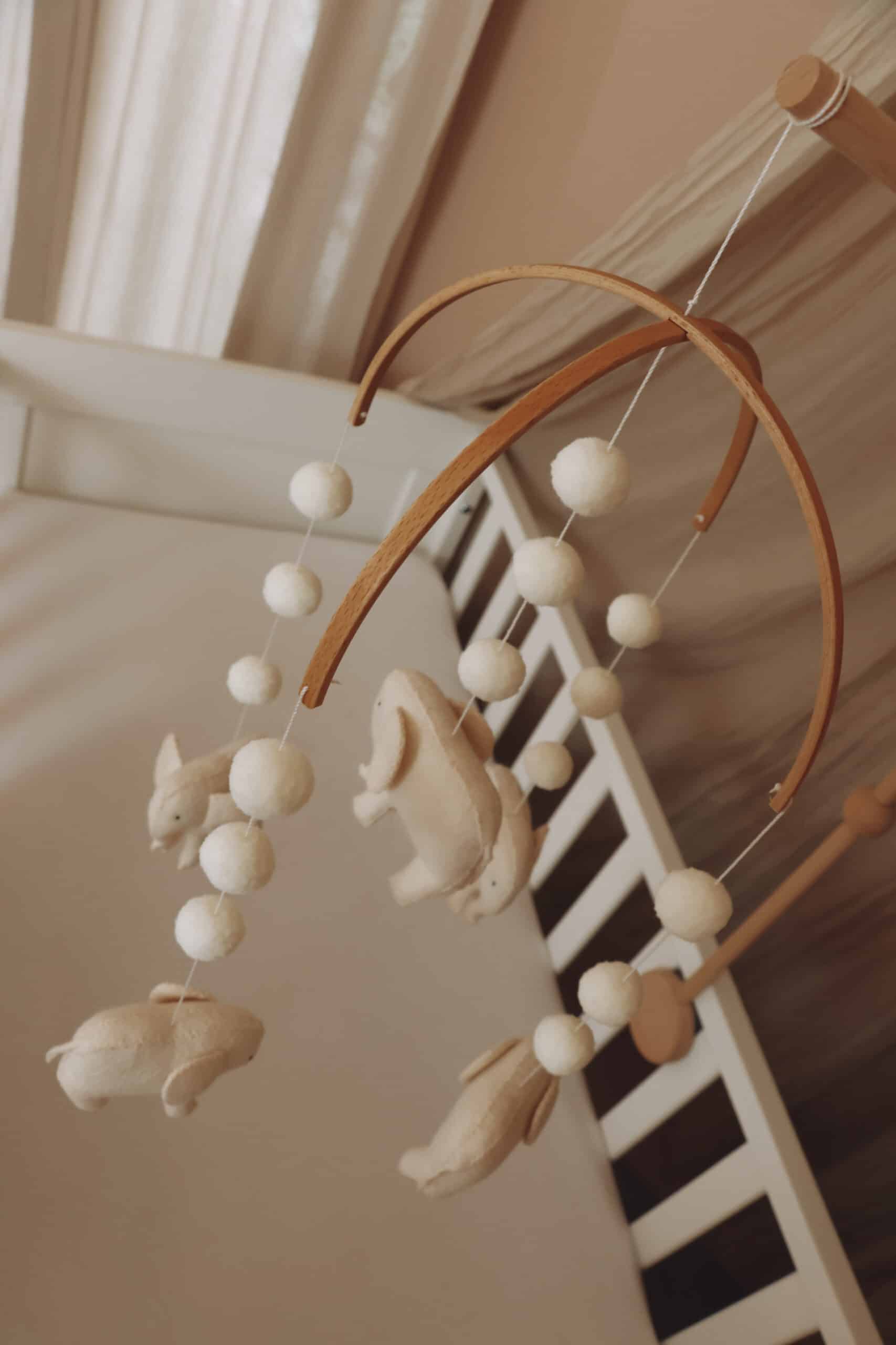 Mobile bébé en feutrine animaux beige, suspendu au-dessus d’un lit à barreaux, décoration chambre enfant