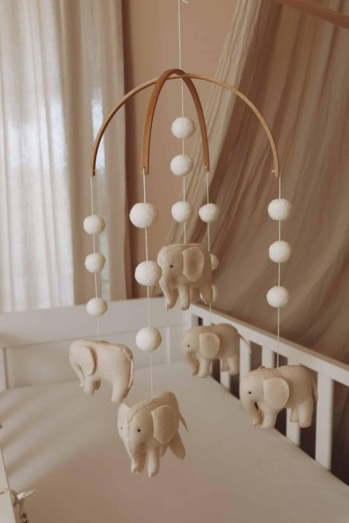 Mobile bébé éléphants en feutrine beige suspendu au-dessus d’un lit enfant dans une chambre douce