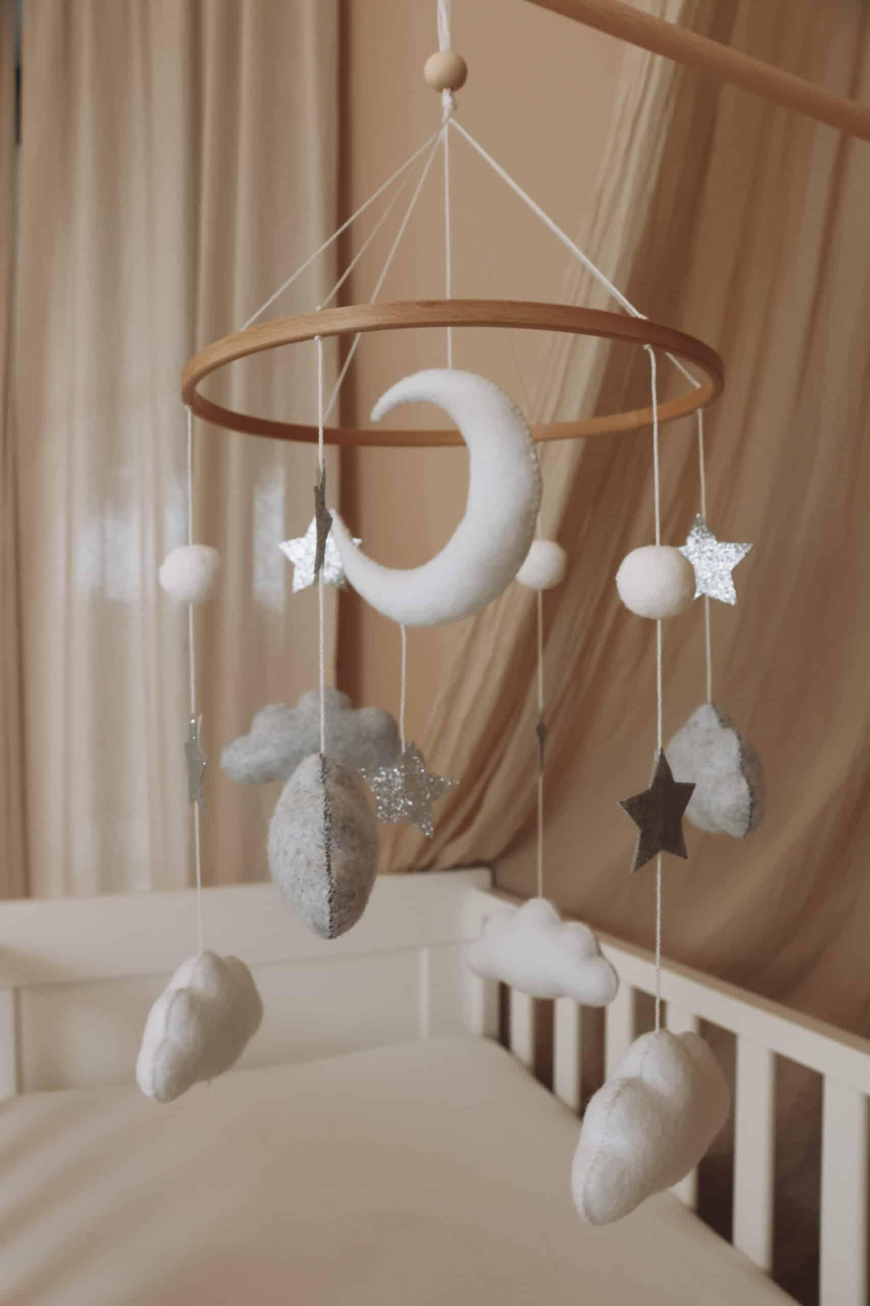 Mobile bébé en feutre avec lune, étoiles et nuages suspendus au-dessus d’un lit enfant