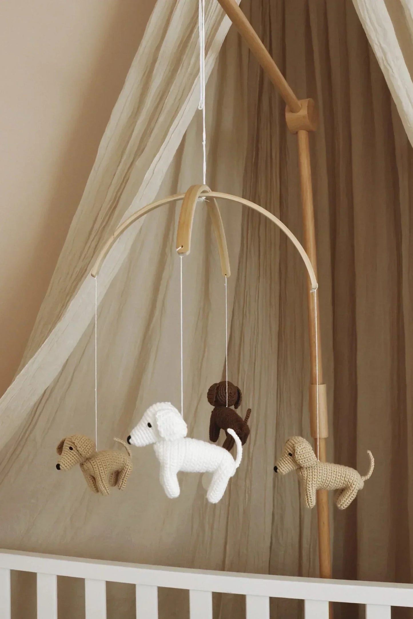 Mobile chien crochet pour bébé suspendu au-dessus d’un lit, décor beige naturel.