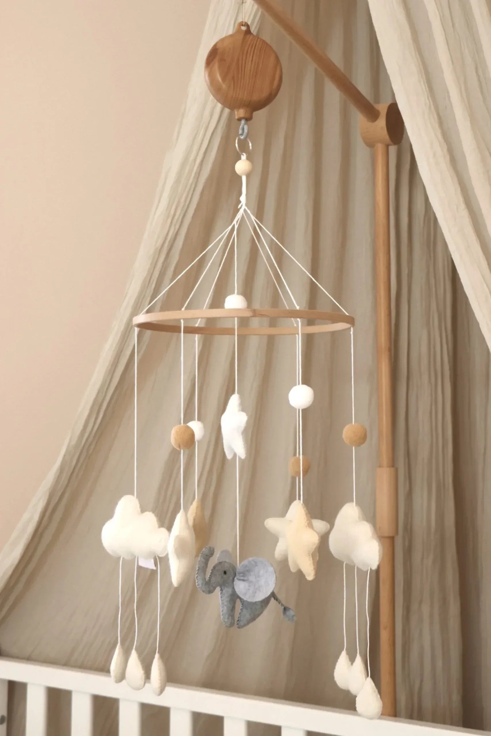 Mobile bébé en laine feutrée avec nuages, étoiles et éléphant, suspendu au-dessus d’un lit.