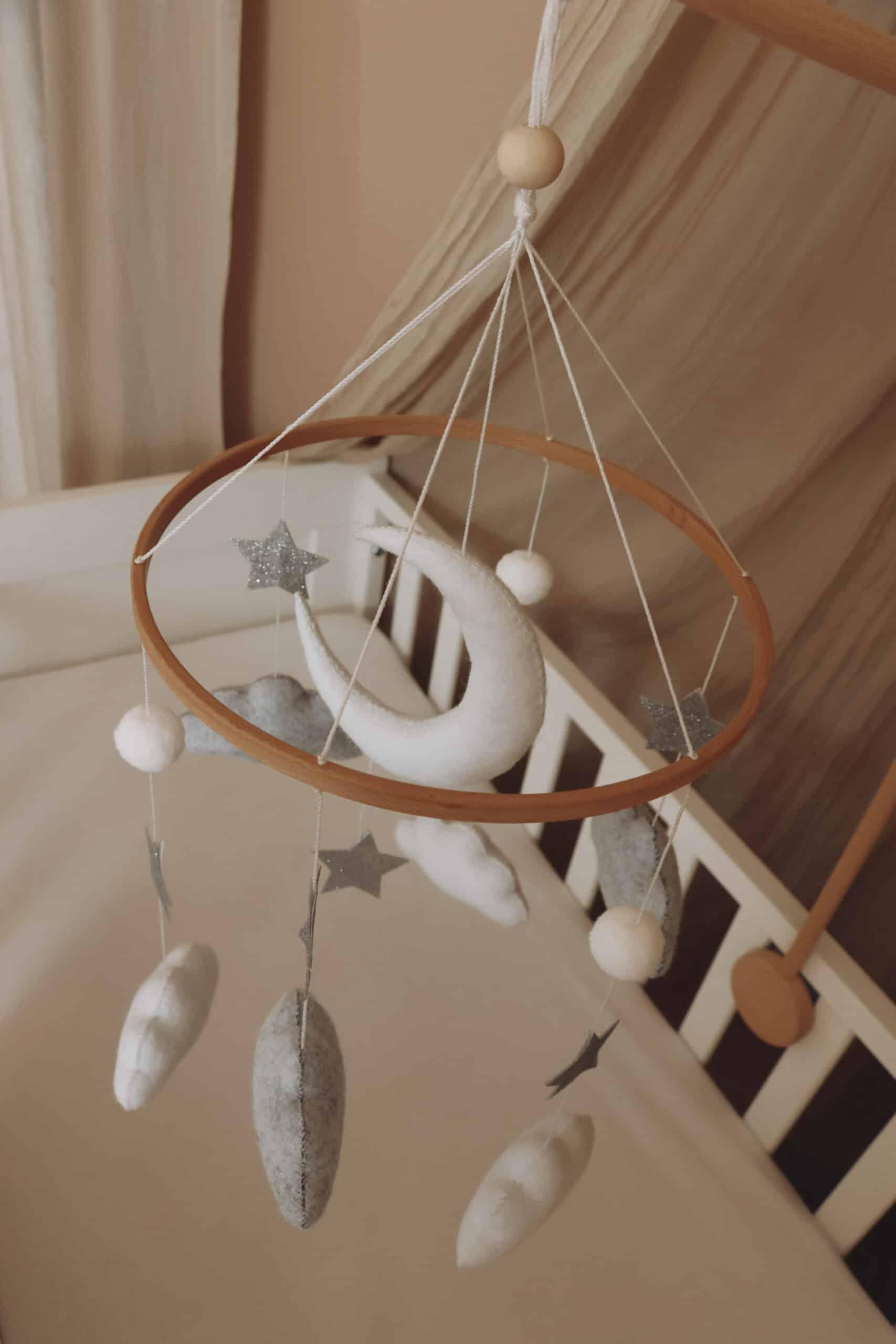 Mobile bébé en feutrine avec lune, étoiles et nuages suspendu au-dessus d’un lit enfant