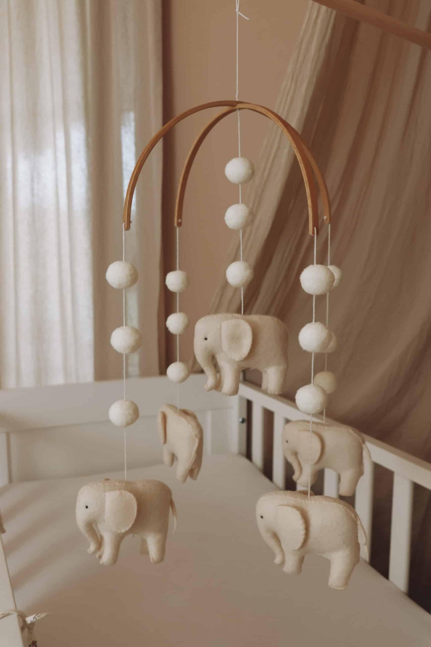 Mobile bébé en feutrine avec éléphants et boules décoratives suspendu au-dessus d’un berceau