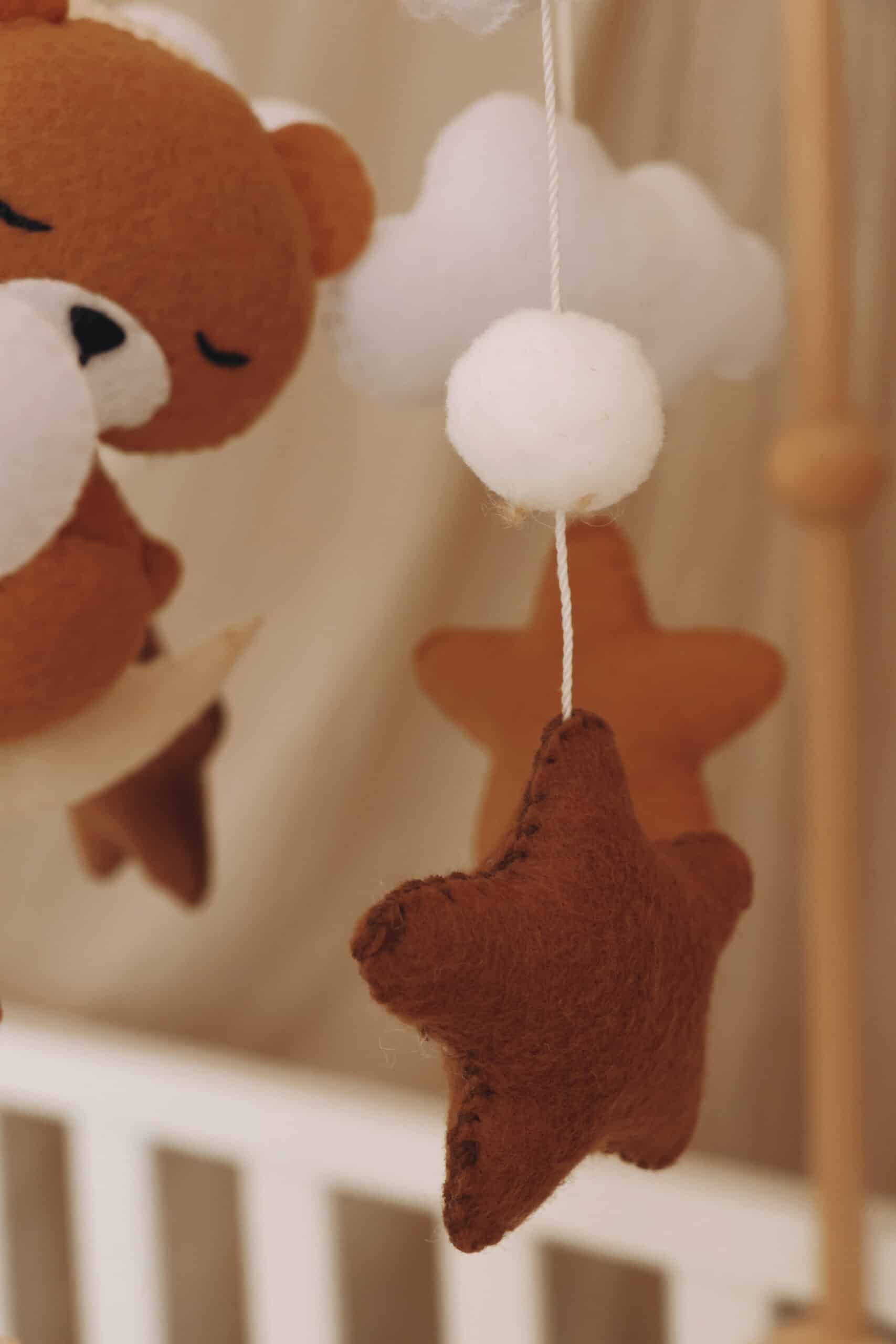 Mobile bébé en feutre avec ours brun, étoiles et nuages décoratifs dans une chambre d'enfant.