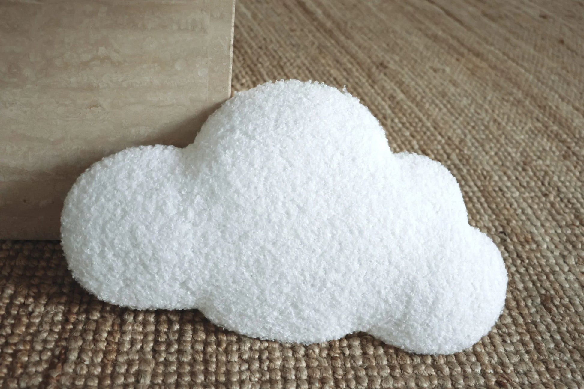 Coussin nuage blanc texturé pour décoration chambre enfant, posé sur tapis en jute
