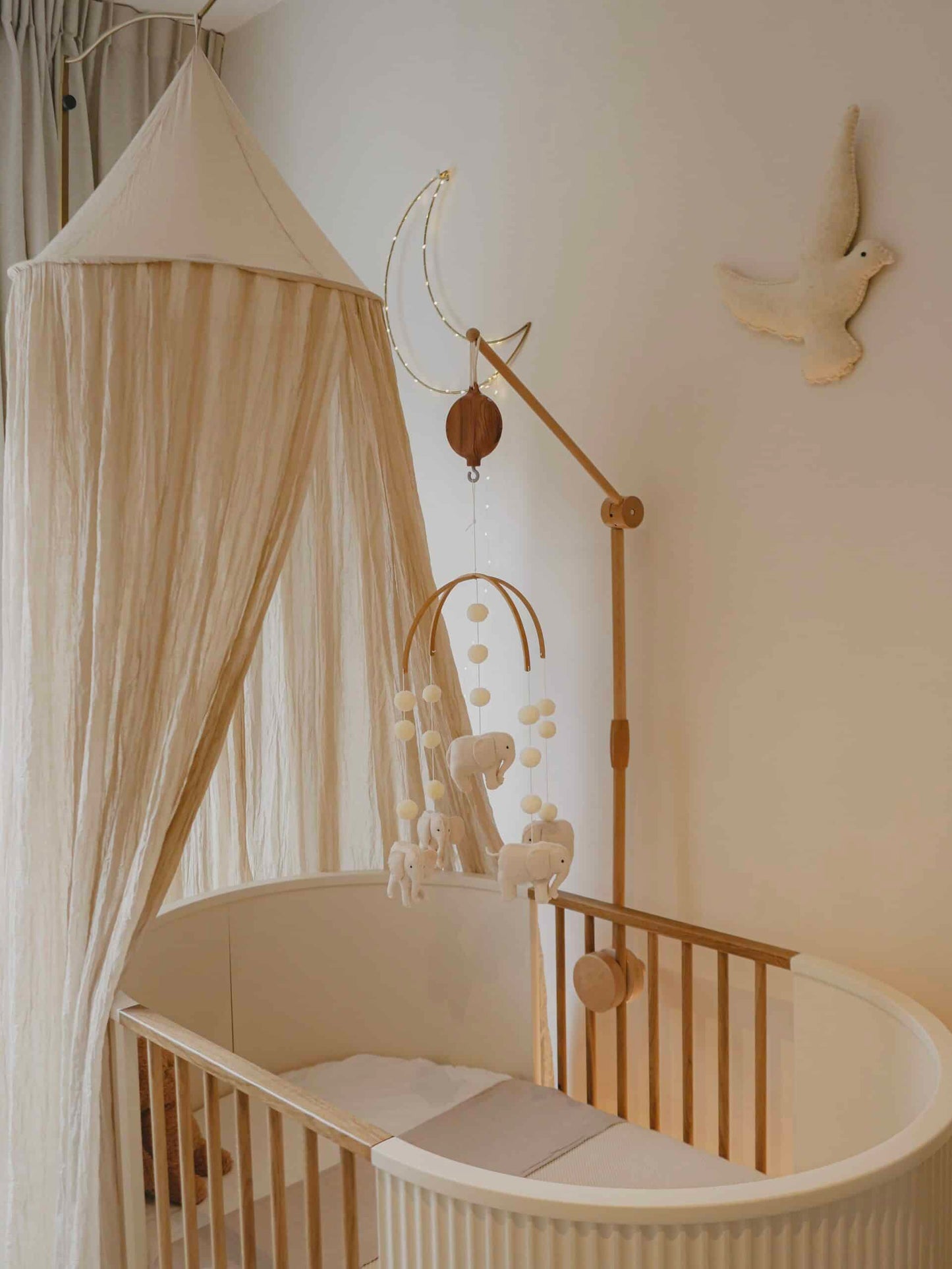 Lit bébé en bois avec ciel de lit beige, mobile animaux, déco murale lune et colombe.