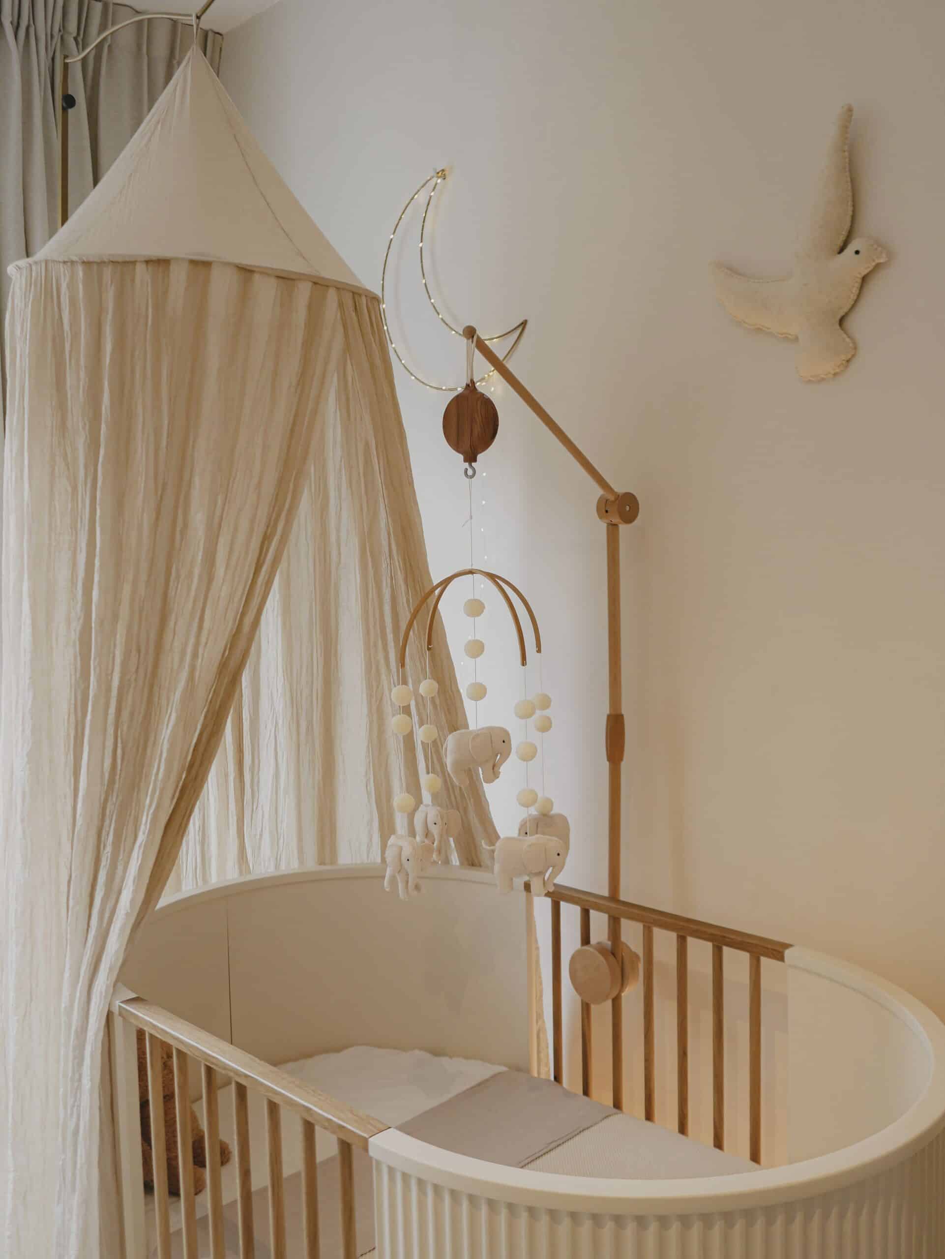 Lit bébé en bois avec ciel de lit beige, mobile animaux, déco murale lune et colombe.